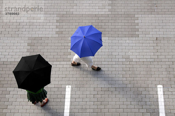 Zwei Frauen mit Regenschirmen gehen über einen Parkplatz.