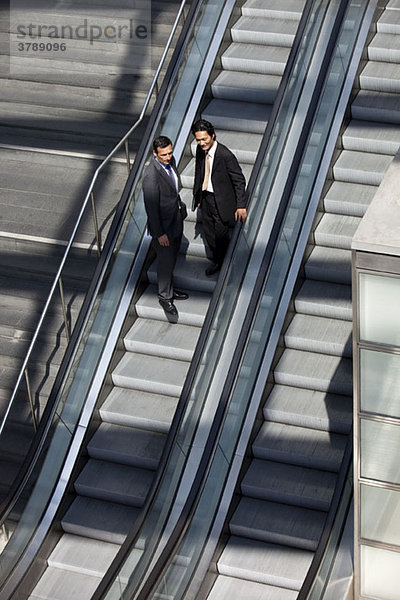 Zwei Geschäftsleute  die eine Rolltreppe runterfahren.