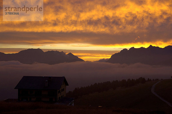 Abendhimmel mit leuchtend orangefarbenen Wolken über Berghütte und Gebirge Hochsavoyen Haute-Savoie Frankreich