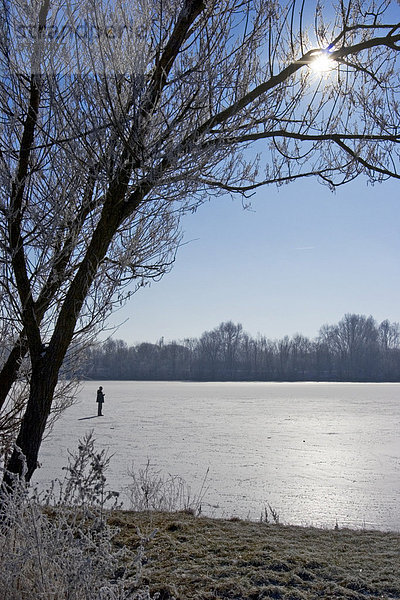 Ein Mann geht über einen zugefrorenen See  starkes Gegenlicht