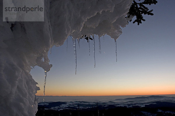 Fernsicht von einem Berg bei Sonnenuntergang im Winter eingerahmt von Eiszapfen