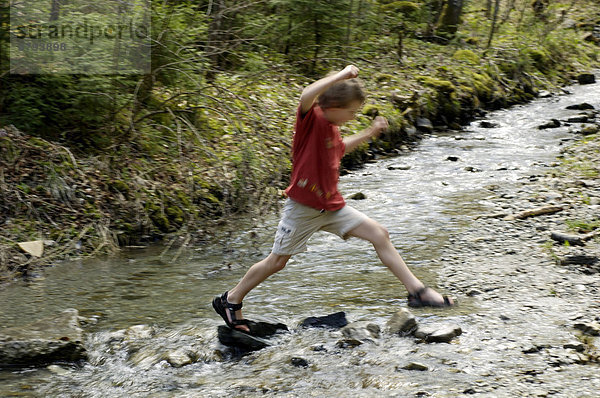 Ein siebenjähriger Junge springt über Bach