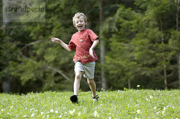 Ein siebenjähriger Junge läuft Wiese hinunter im Frühling