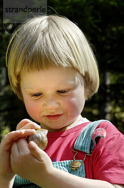 Ein dreijähriges Mädchen untersucht eine Schnecke