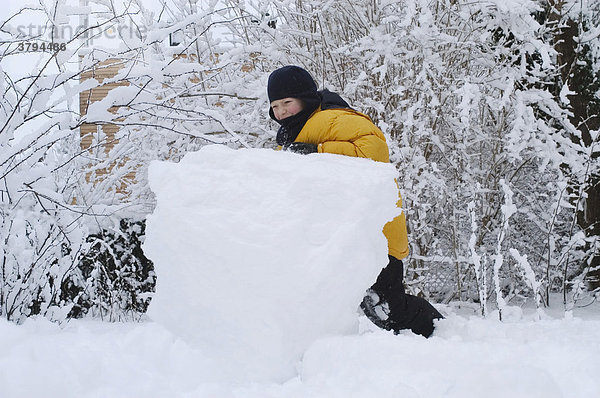 Kleiner Junge 8 Jahre wälzt Schneekugel um einen Schneeman zu bauen
