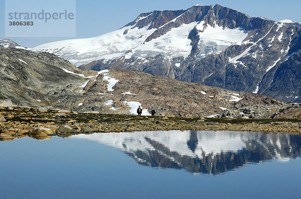 Zwei einsame Wanderer vor Berg mit Gletscher Spiegelung im See bei Tiniteqilaaq Ostgrönland