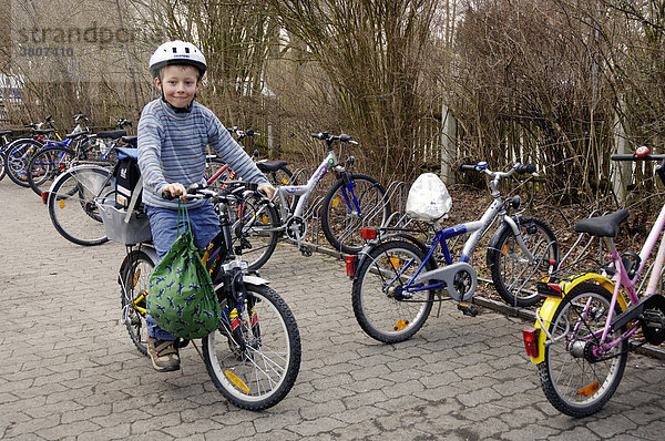 Acht Jahre alter Junge mit Helm am Fahrradständer auf dem Fahrrad