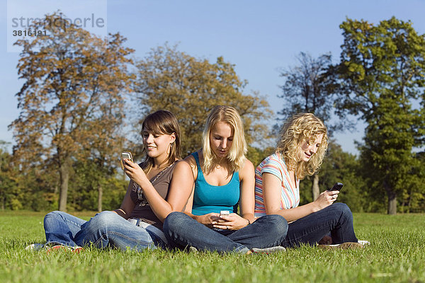 Drei Freundinnen sitzen in einem Park und schreiben SMS