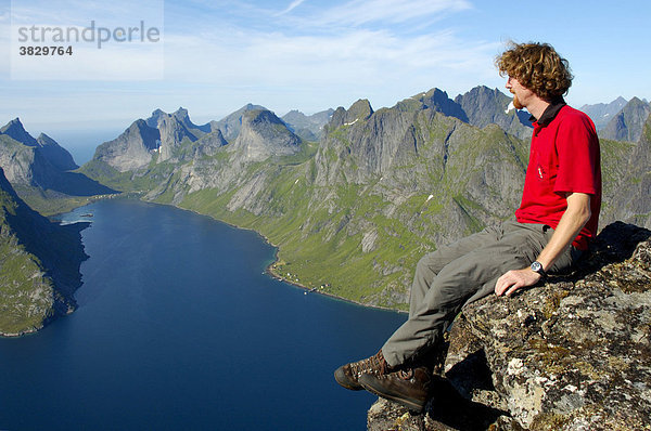 MR Bergsteiger genießt die Aussicht vom Gipfel Navaren auf spitze Berge mit Fjord Kjerkfjorden Moskenesöya Lofoten Norwegen