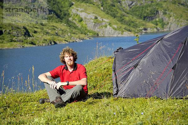 MR Junger Mann sitzt vor seinem Zelt in der Wildnis von Moskenesöy mit Agvatnet Lofoten Norwegen