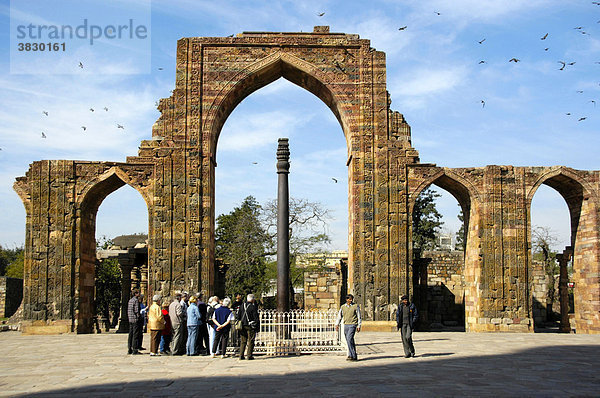 Gruppe von Touristen steht um die eiserne Säule mit Ruinen Bögen einer Moschee Qtab Minar Delhi