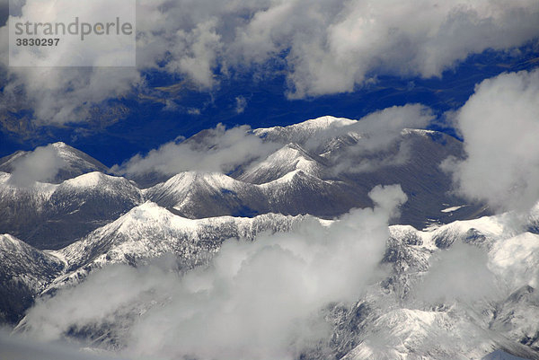 Blick von oben auf schneebedeckte Gebirgszüge umgeben von Wolken Tibet China