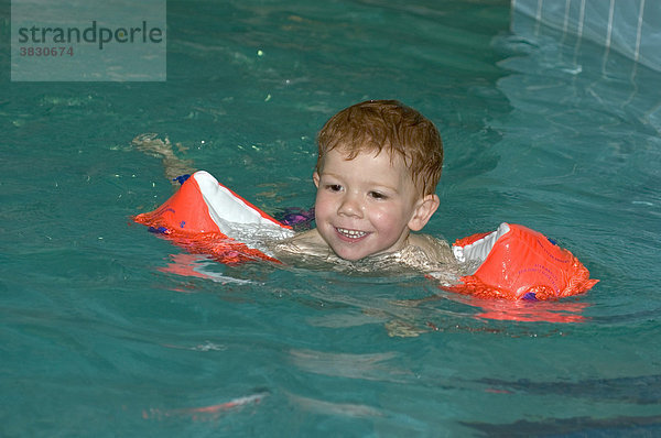 Kind schwimmt mit Schwimmflügel im Schwimmbad