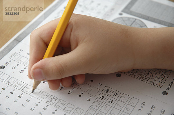 Hausaufgaben: Hand mit gelbem Bleistift  Blatt mit Rechenaufgaben