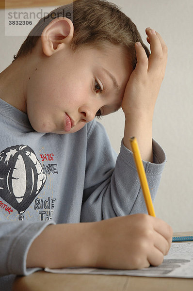 Junge in blauem Shirt sitzt am Tisch und arbeitet mit Papier und Bleistift