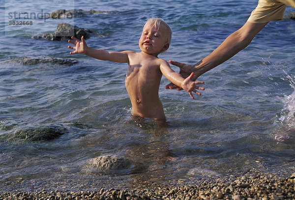 Einjähriger steht im Wasser und ist am Umfallen. Hand fängt ihn auf - Mallorca - Spanien