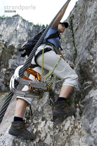 Klettererin auf steilem Klettersteig bei Erwald (Österreich) mit Sicherheitkarabinern an Stahlseil im Vordergrund.