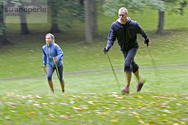 Zwei Nordic Walker mit Stöcke und sportliche Kleidung laufend auf einer grünen Wiese im Englichen Garten in München