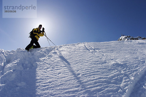 Skitourengeher am Berg mit Skistöcken und gelber Jacke in der schneebedeckten Winterlandschaft mit blauem Himmel an der Scheinbergspitze unweit von Schloss Linderhof in Deutschland