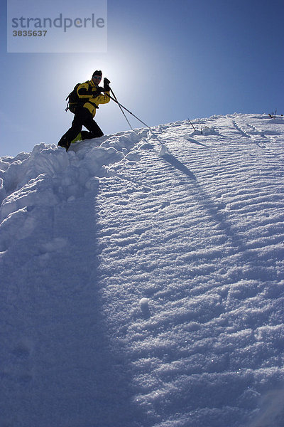 Skitourengeher am Berg mit Skistöcken und gelber Jacke in der schneebedeckten Winterlandschaft mit blauem Himmel an der Scheinbergspitze unweit von Schloss Linderhof in Deutschland
