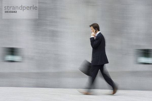 Mitzieher eines schnell laufenden Geschäftsmannes mit Aktentasche in der Hand vor einer hohen Betonwand in München