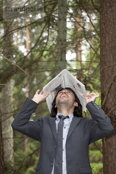 Junger  gut gelaunter Geschäftsmann mit Zeitung auf dem Kopf im Wald