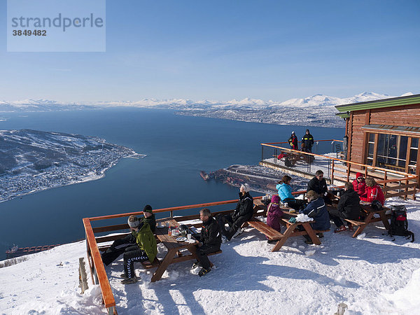 Wintersportler sitzen hoch über dem Ofotfjord am Berg Fagernes-Fjellet im Schnee und genießen das sonnige Wetter in Narvik  Nordland  Norwegen  Europa