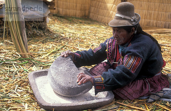 Ältere Frau der Aymara-Ureinwohner reibt mit einem Mahlstein Getreide zu Mehl  Schilfinsel aus Totora Schilf  Titicacasee  Peru  Südamerika