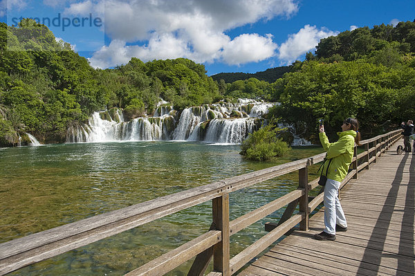 Touristin fotografiert auf Holzbrücke den Wasserfall  Nationalpark Krka Wasserfälle  Gespanschaft Sibenik-Knin  Kroatien  Europa