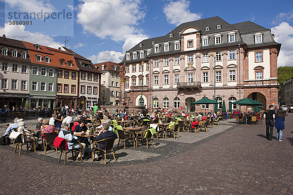 Touristen sitzen in der Sonne auf dem alten Marktplatz mit dem Herkulesbrunnen  hinten das Rathaus  Neckar  Heidelberg  Baden-Würtemberg  Deutschland  Europa
