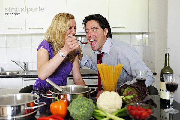 Junges Paar beim Essen zubereiten  sie gibt ihm einen Löffel zum Probieren