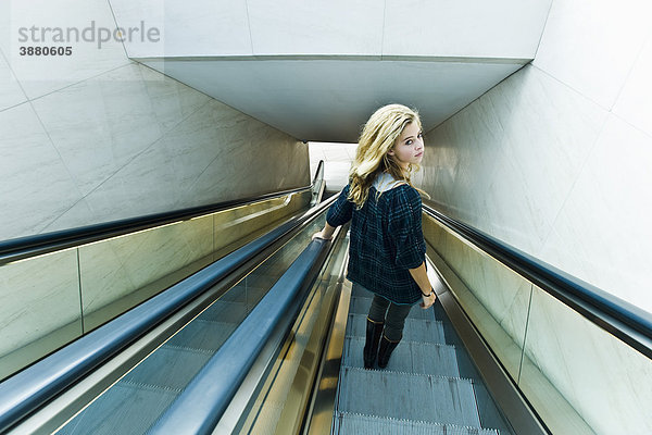 Teenagerin auf Rolltreppe  Blick über die Schulter zur Kamera