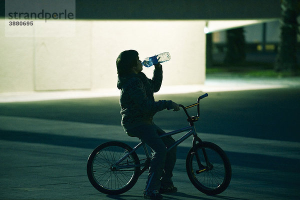 Junge sitzt auf dem Fahrrad und trinkt aus einer Flasche Wasser.