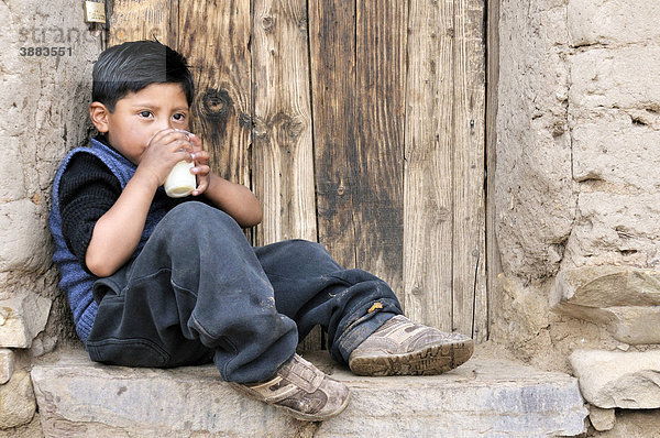 Junge sitzt mit einem Becher Milch an einer Mauer  Bolivianisches Hochland Altiplano  Departamento Oruro  Bolivien  Südamerika
