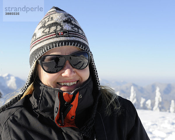 Junge Frau mit Norwegermütze und Sonnenbrille in einer Winterlandschaft