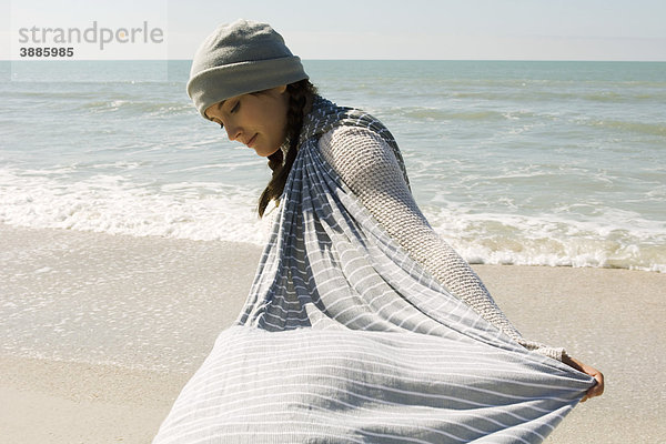 Teenagermädchen geht am Strand spazieren  hält einen Schal im Wind.