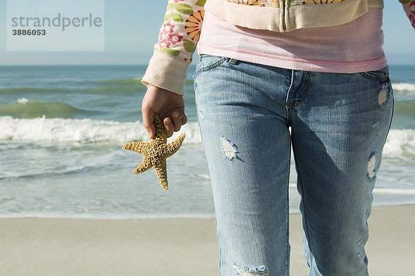 Teenagerin  die am Strand spazieren geht und Seesterne trägt.