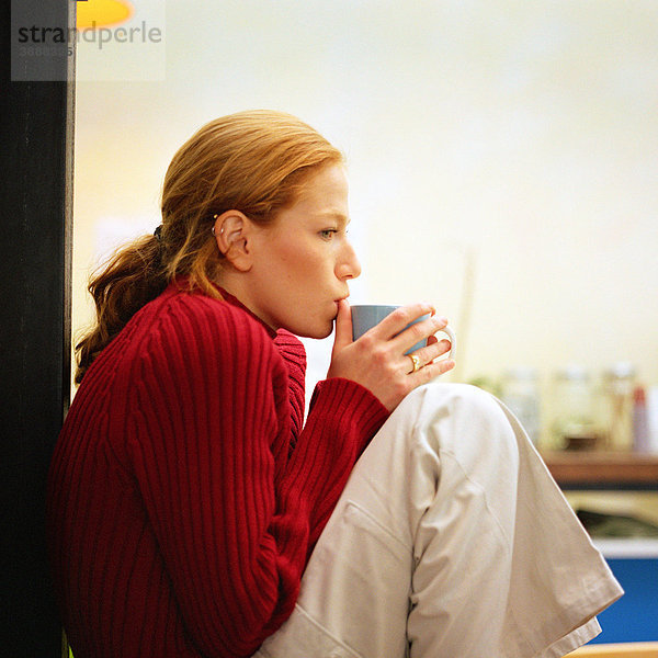 Junge Frau sitzend trinkend aus der Tasse  Seitenansicht