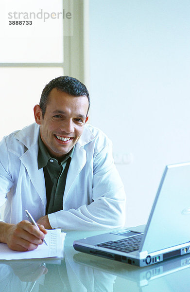 Arzt sitzend mit Laptop  Schreiben mit Stift auf Papier  Smiliing