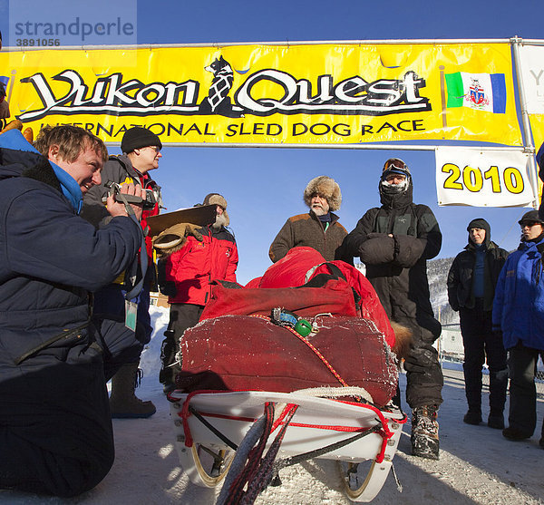 Hundeschlittenführer Normand Casavant steht an seinem beladenen Schlitten  im Gespräch mit der Rennleitung Hans Oettli nach der Ankunft in Dawson City  Yukon Quest 1000-Meilen Internationales Schlittenhunderennen 2010  Yukon Territory  Kanada