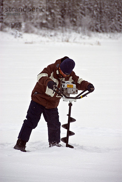 Angler mit Eisbohrer  bohrt für das Eisfischen ein Loch in einen gefrorenen See  Winter  Yukon Territory  Kanada