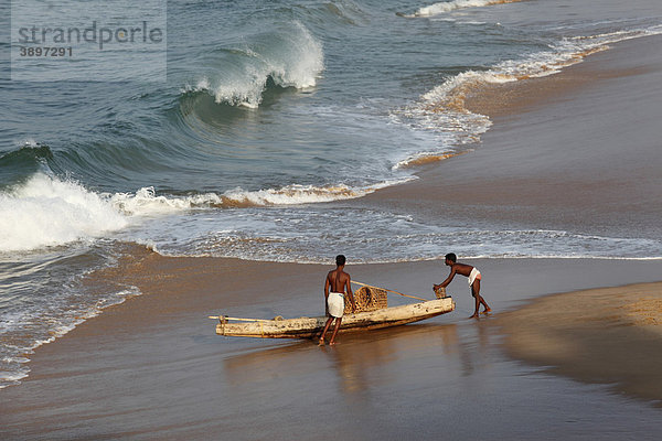 Zwei Einheimische mit einfachem Fischerboot an Strand südlich von Kovalam  Malabarküste  Malabar  Kerala  Südindien  Indien  Asien