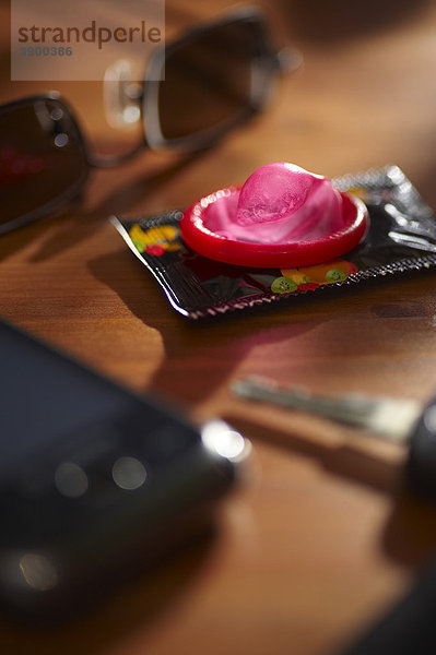 Ein Kondom liegt auf einem Tisch neben einem Handy  einem Autoschlüssel und einer Sonnenbrille  Symbolbild Untreue