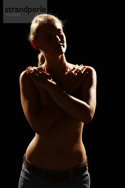 Junge Frau bedeckt den nackten Oberkörper mit verschränkten Armen  Gegenlicht
