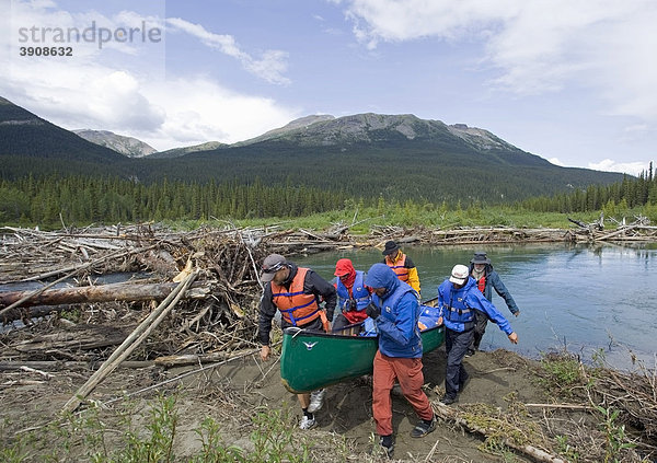 Männer portagieren  tragen ein Kanu über Land um ein Hindernis zu umgehen  dahinter eine Blockade durch Baumstämme  oberer Liard River Fluß  Yukon Territory  Kanada