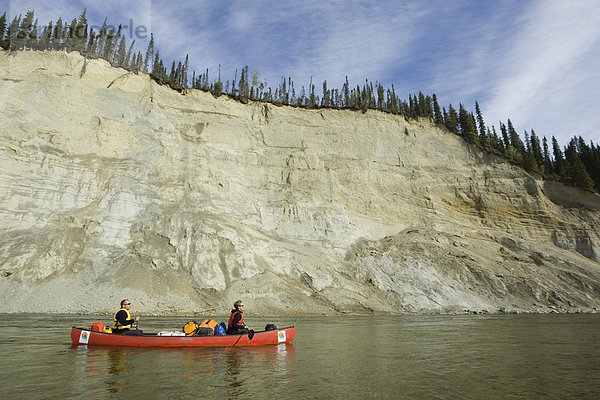 Paar  Mann und Frau paddeln ein Kanu  Kanufahren  vom Fluss geformte Landschaft  Erosion in weichem Sandstein  hohes eingeschnittenes Flussufer  Klippe  oberer Liard River Fluss  Yukon Territory  Kanada