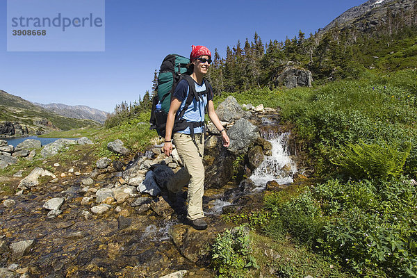 Junge Frau überquert Bach  kleiner Wasserfall  Wandern  Wanderin mit Rucksack  historischer Chilkoot Pass  Chilkoot Trail  alpine Tundra  Yukon Territorium  British Columbia  BC  Kanada