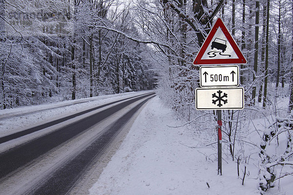 Warnschilder im Winter  Verkehrsschilder warnen vor Schleudergefahr bei Glatteis und Schnee auf vereister Straße im Wald  Tangstedt  Schleswig-Holstein  Deutschland  Europa