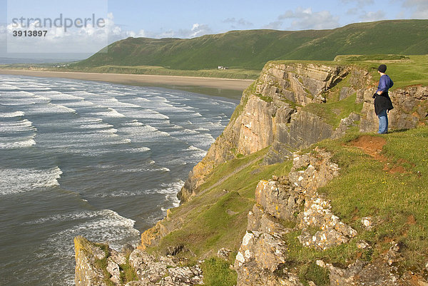 Frau steht auf Klippe  schaut auf Wellen und Strand  Rhossili Beach  Gower Peninsula  Wales  Großbritannien  Europa