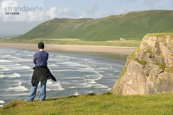 Frau steht auf Klippe  schaut auf Wellen und Strand  Rhossili Beach  Gower Peninsula  Wales  Großbritannien  Europa